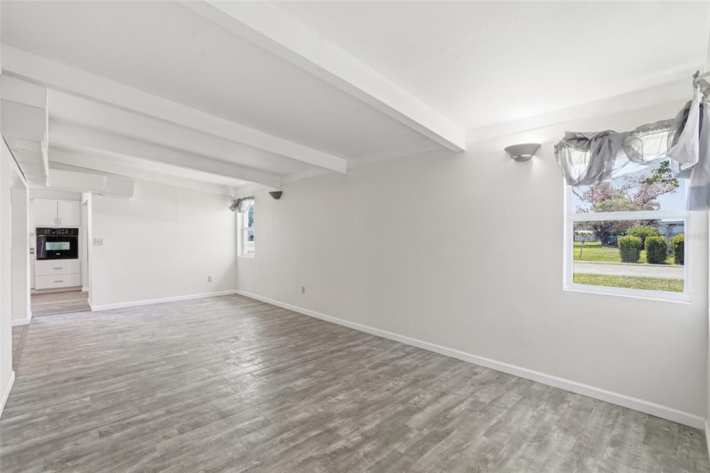 An empty room with white walls, exposed ceiling beams, gray wood-look flooring, and a window — 503 MYRTLE STREET, PUNTA GORDA, FL
