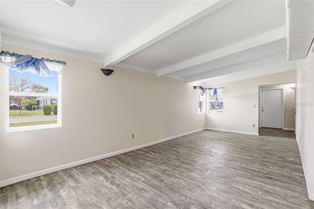 An empty room with white walls, exposed ceiling beams, and gray wood-look flooring — 503 MYRTLE STREET, PUNTA GORDA, FL