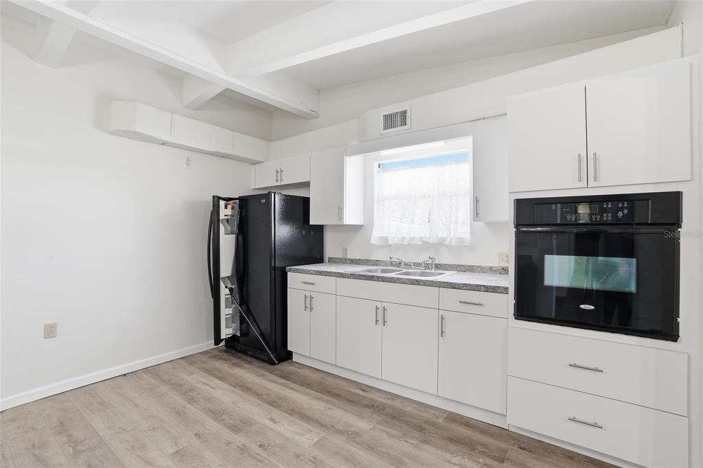 A kitchen features white cabinets, a black refrigerator, a built-in oven, and wood-look flooring — 503 MYRTLE STREET, PUNTA GORDA, FL