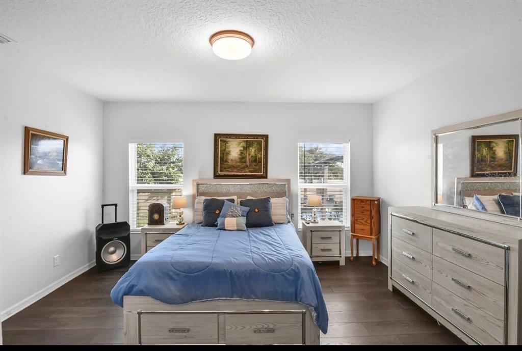 A bedroom features a bed with a blue comforter, a dresser with a mirror, and windows — 9213 HALSEY DR, GROVELAND, FL