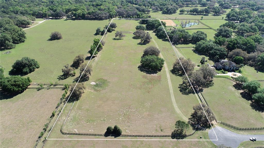 An aerial view shows a large, fenced grassy pasture with scattered trees and a house — TBD SW 104TH  ST ROAD, OCALA, FL