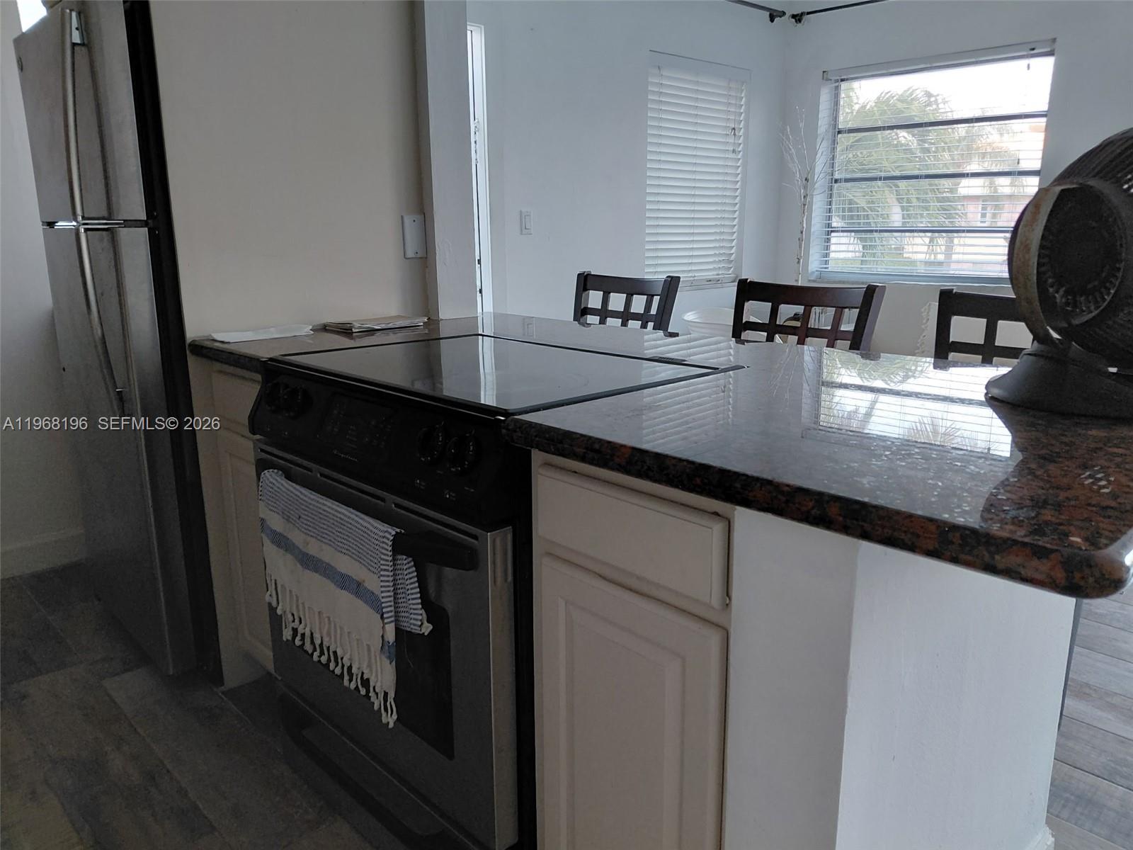 A kitchen features a stainless steel stove, granite countertops, and a view of dining chairs — 1334 Euclid Ave # 7, Miami Beach FL 33139, MIAMI BEACH, FL