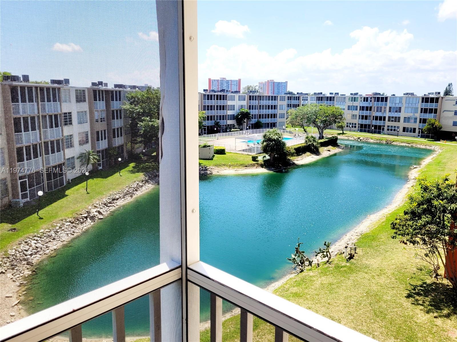 A view from a screened balcony overlooking a pond and apartment buildings — 1700 NE 191st St # 402, Miami FL 33179, MIAMI, FL