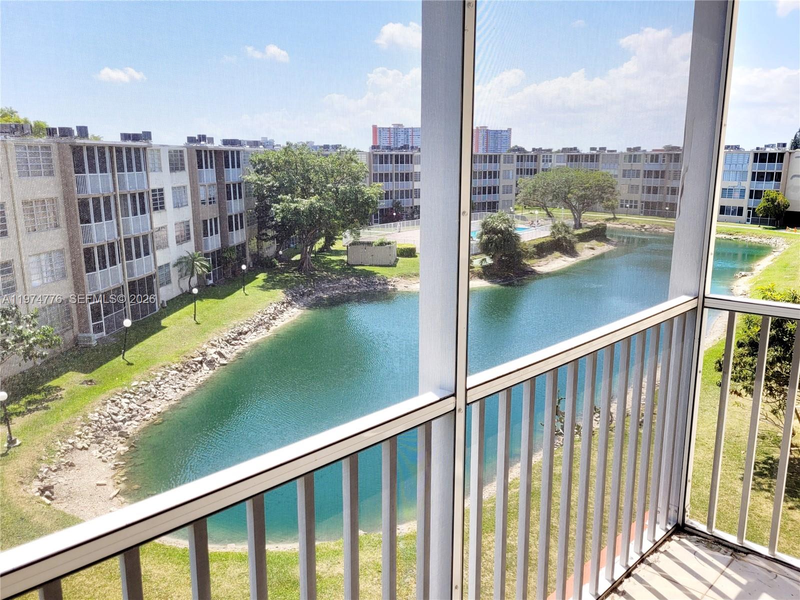 A view from a screened balcony overlooking a pond and apartment buildings — 1700 NE 191st St # 402, Miami FL 33179, MIAMI, FL