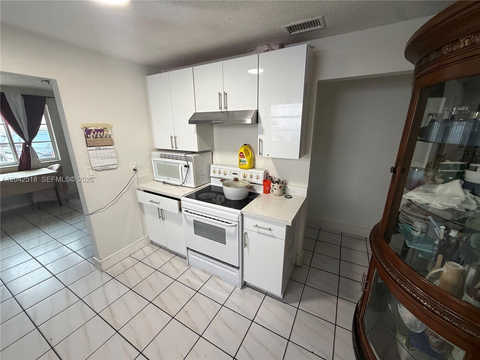 A kitchen features white cabinets, a white stove, a microwave, and light-colored tiled flooring — 1717 NW 16th St, Miami FL 33125, MIAMI, FL