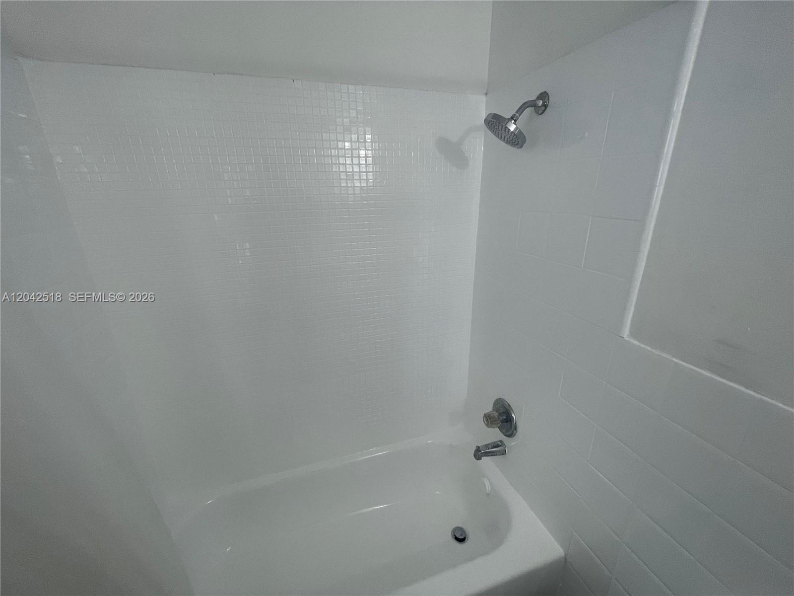 A white tiled bathtub and shower combination with a chrome showerhead and faucet — 1717 NW 16th St, Miami FL 33125, MIAMI, FL