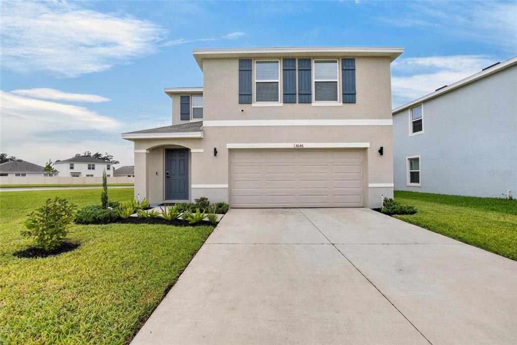 A two-story suburban house with a beige stucco exterior, a garage, and a concrete driveway — 13646 MOUNT IVY COURT, DADE CITY, FL