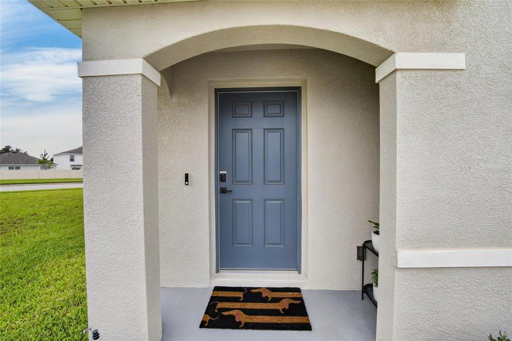 A blue front door with a dachshund-themed doormat sits under a covered porch entrance — 13646 MOUNT IVY COURT, DADE CITY, FL