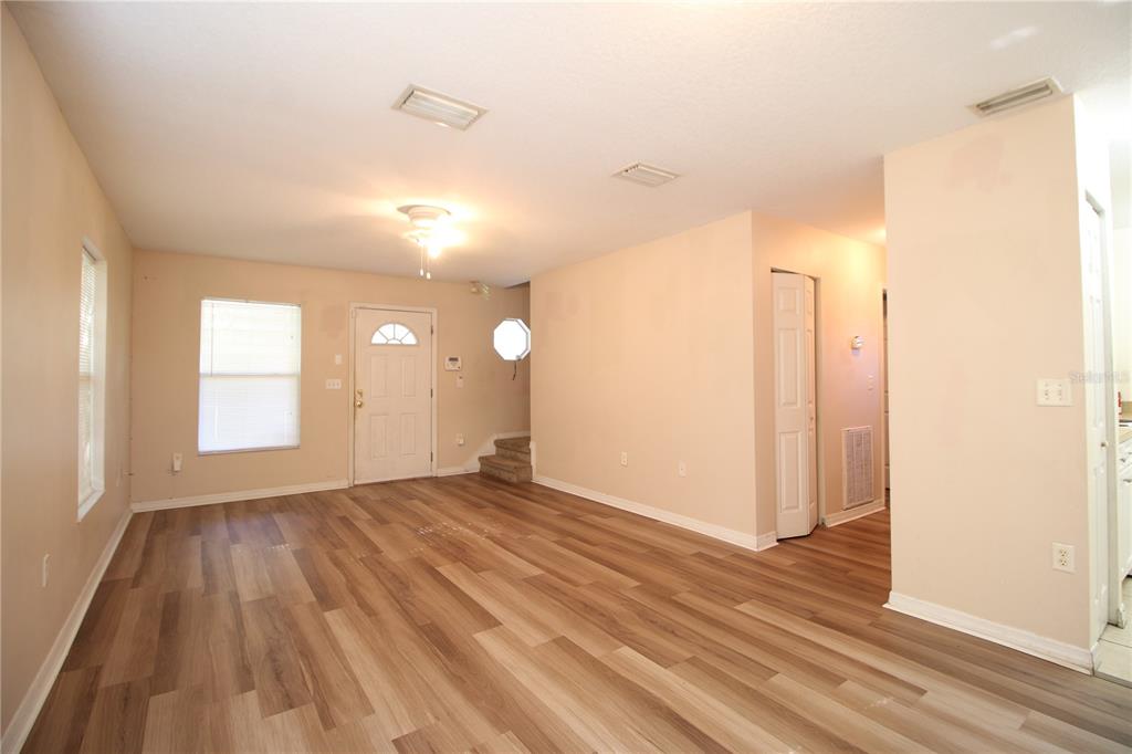 An empty living room features light wood-look flooring, beige walls, a front door, and stairs — 720 NEWTON AVENUE S, ST PETERSBURG, FL