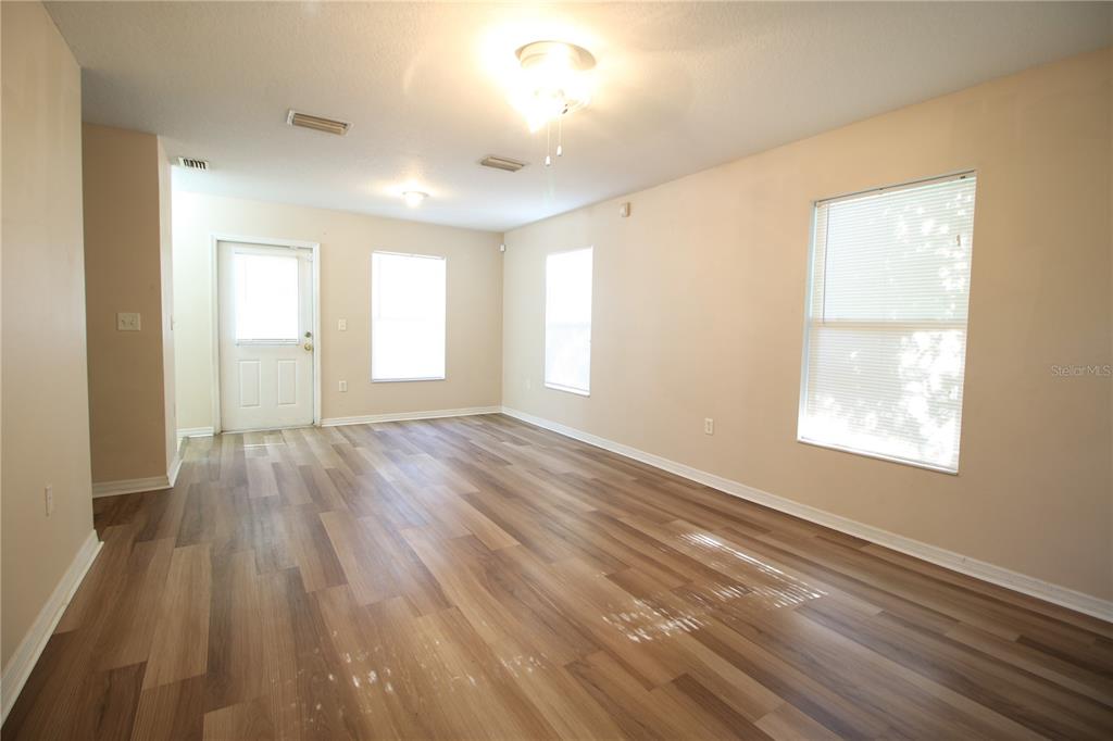 An empty living room features light-colored walls, wood-look flooring, a ceiling fan, and several windows — 720 NEWTON AVENUE S, ST PETERSBURG, FL