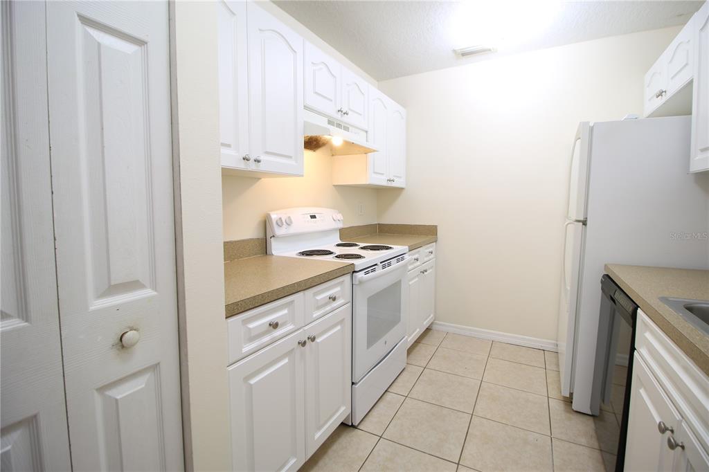 A galley-style kitchen features white cabinets, tan countertops, white appliances, and light-colored tile flooring — 720 NEWTON AVENUE S, ST PETERSBURG, FL