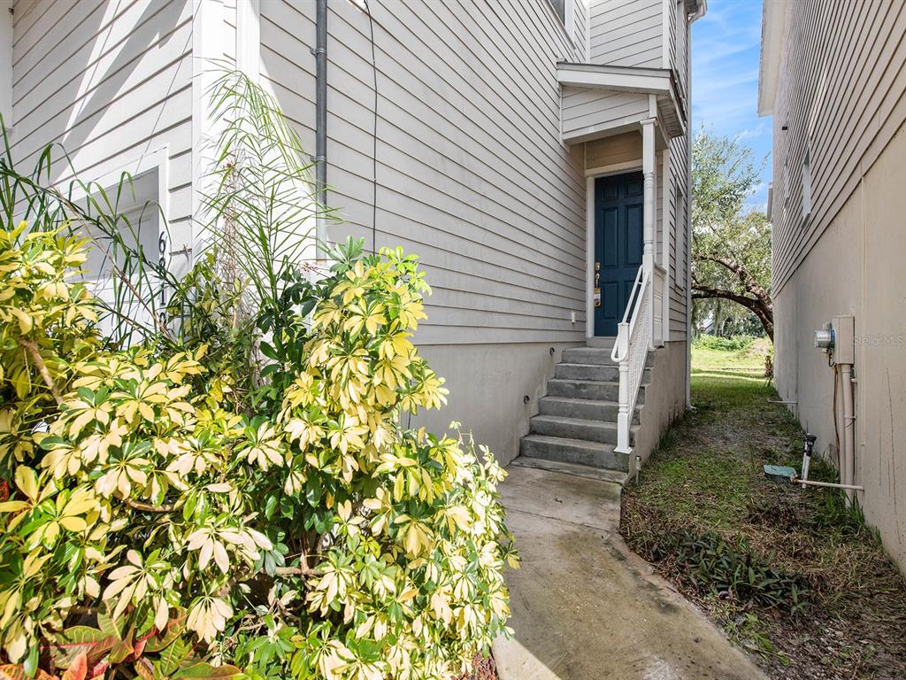 A concrete walkway leads to a set of stairs and a blue door on a house — 6810 KISSIMMEE STREET S, TAMPA, FL