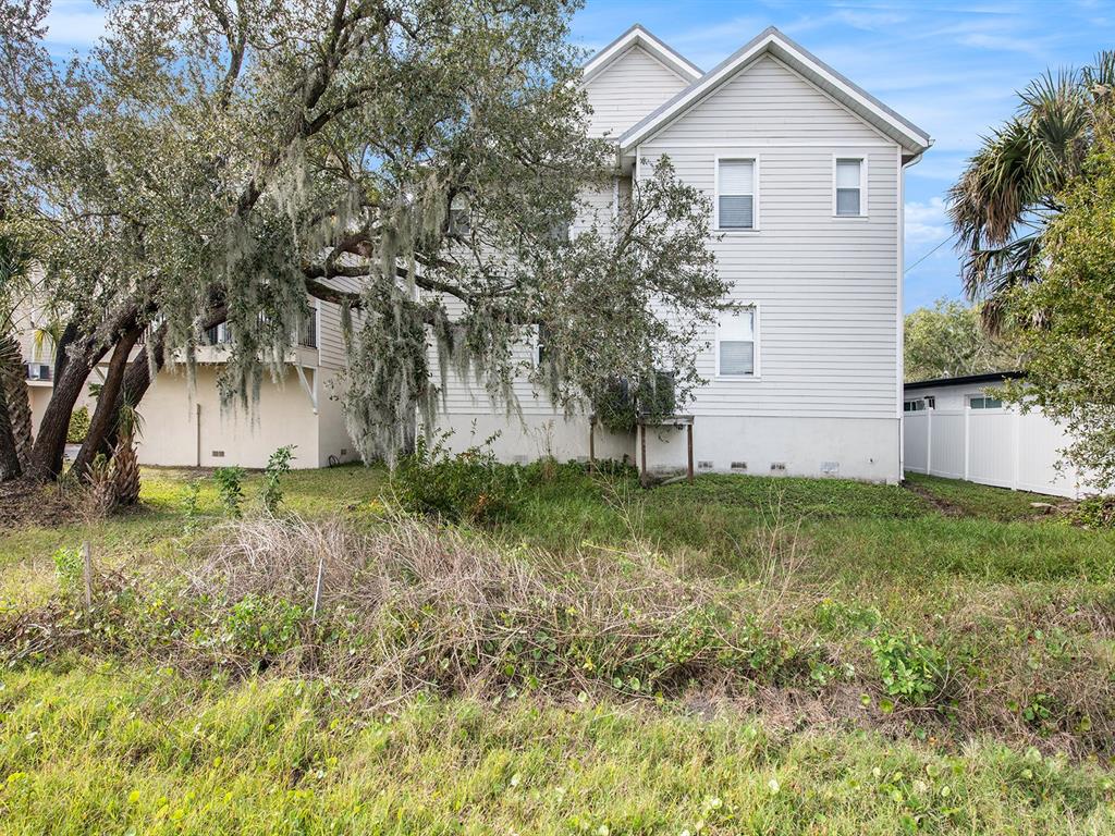 A two-story house with light-colored siding stands behind a grassy, overgrown yard and trees — 6810 KISSIMMEE STREET S, TAMPA, FL