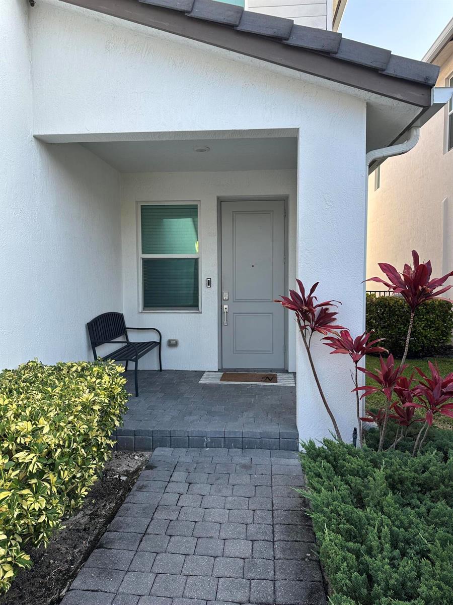 A paved walkway leads to a covered front porch with a gray door and bench — 1131 Verde Court, Deerfield Beach FL 33064, DEERFIELD BEACH, FL