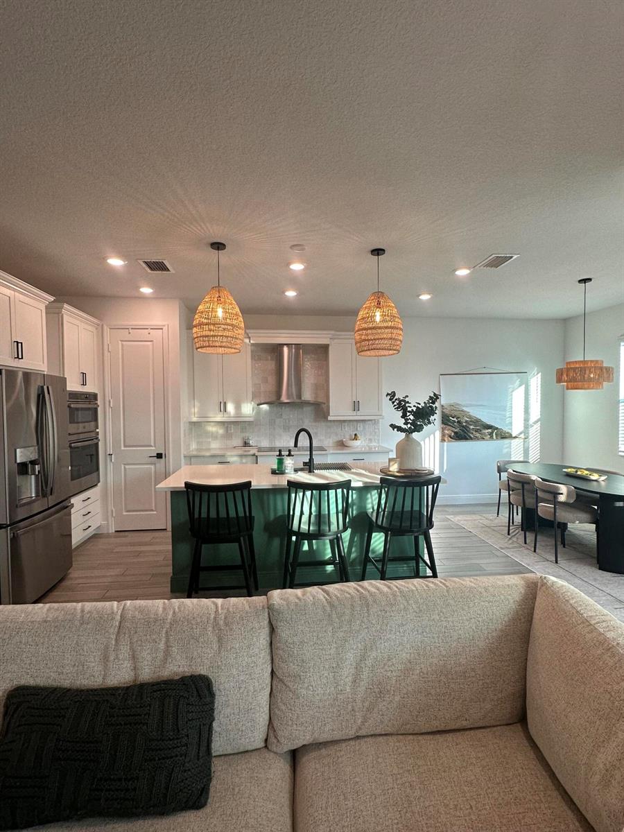 A kitchen with a green island, white cabinets, and woven pendant lights overlooks a dining area — 1131 Verde Court, Deerfield Beach FL 33064, DEERFIELD BEACH, FL