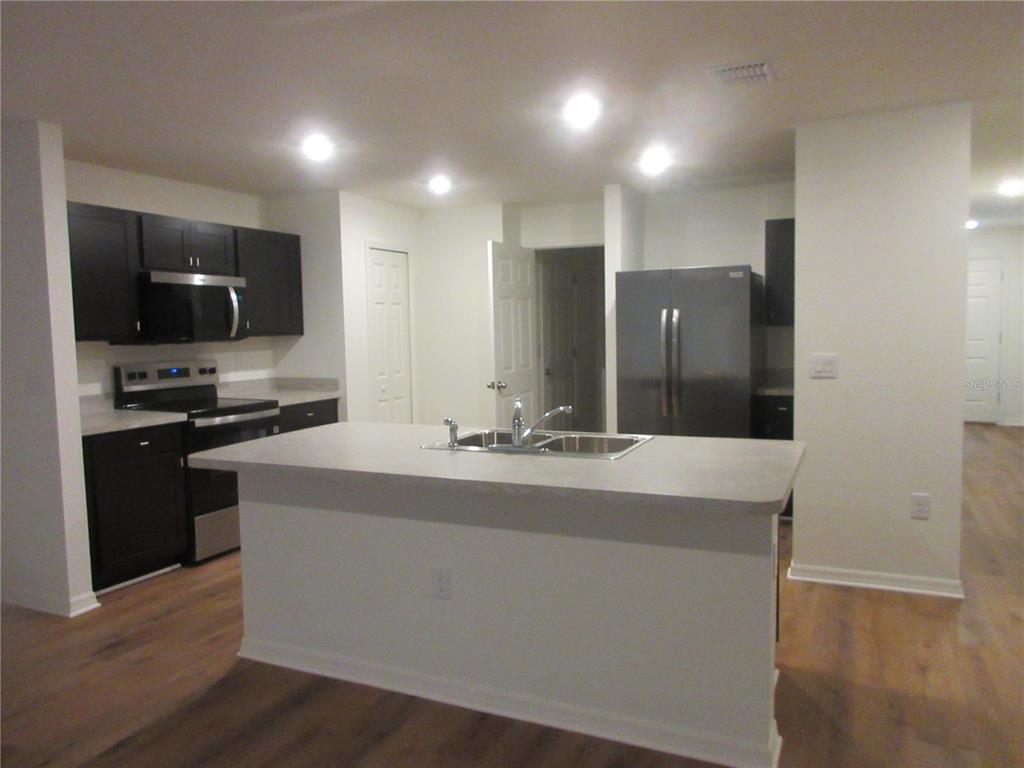 A modern kitchen features dark cabinets, stainless steel appliances, and a central island with sink — 13130 SW 78TH CIRCLE, OCALA, FL
