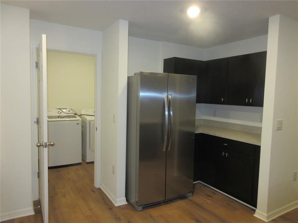A kitchen with dark cabinets and a stainless steel refrigerator next to a laundry room — 13130 SW 78TH CIRCLE, OCALA, FL