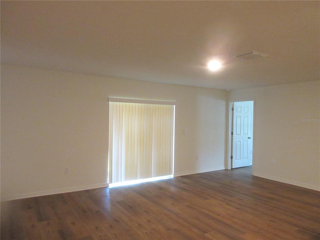An empty room with wood-look flooring, light-colored walls, and a sliding glass door — 13130 SW 78TH CIRCLE, OCALA, FL