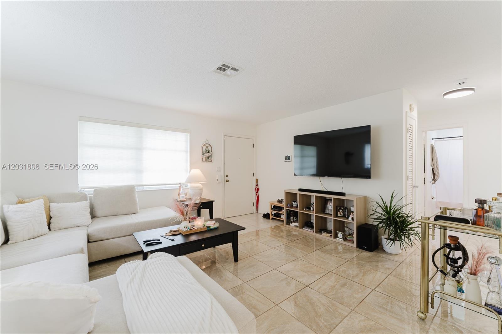 A living room features a sectional sofa, a wall-mounted television, and beige tile flooring — 2604 NW 48th St, Tamarac FL 33309, TAMARAC, FL