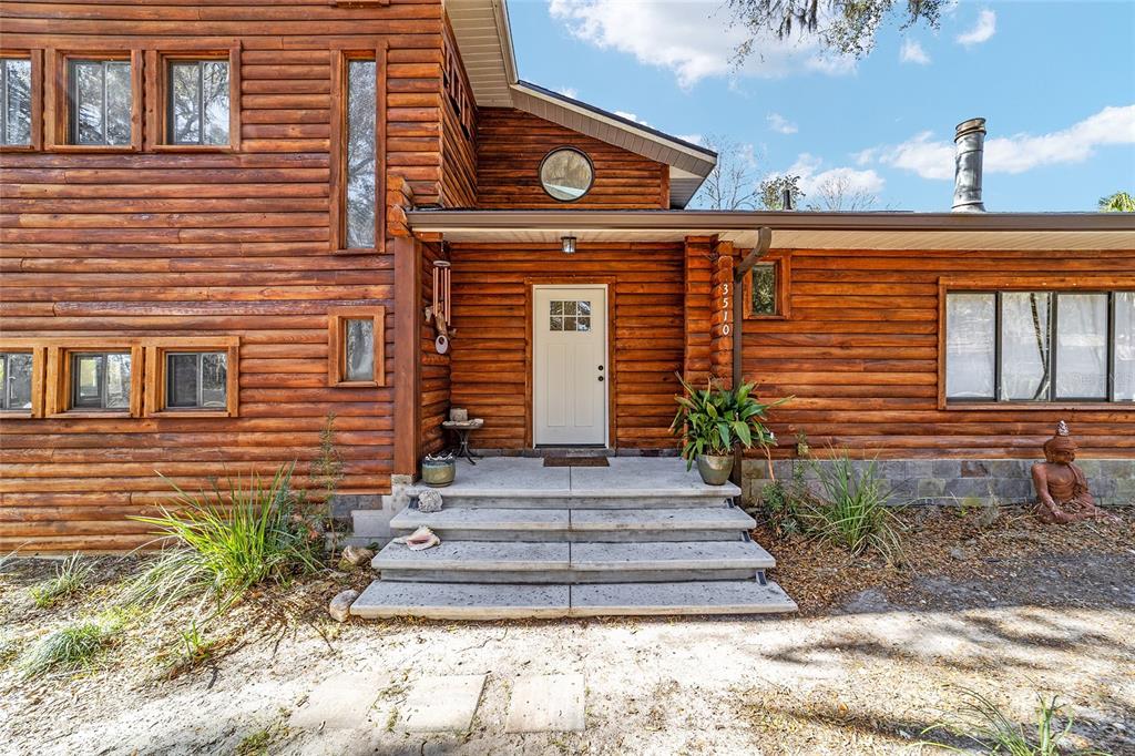 A log cabin exterior features a white front door, concrete steps, and multiple windows — 3510 SW 5TH COURT, OCALA, FL