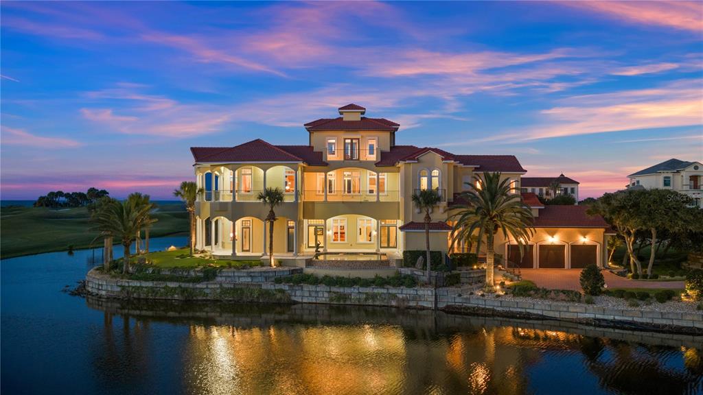 A large multi-story Mediterranean-style house sits on a waterfront lot at sunset — 501 GRANADA DRIVE, PALM COAST, FL