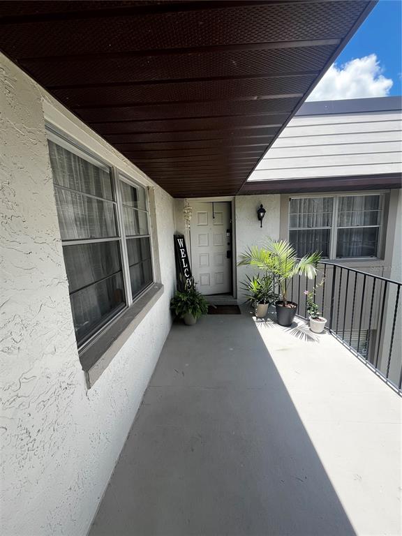 An outdoor covered walkway leads to a front door with a welcome sign and plants — 110 WINDTREE LANE UNIT 202, WINTER GARDEN, FL