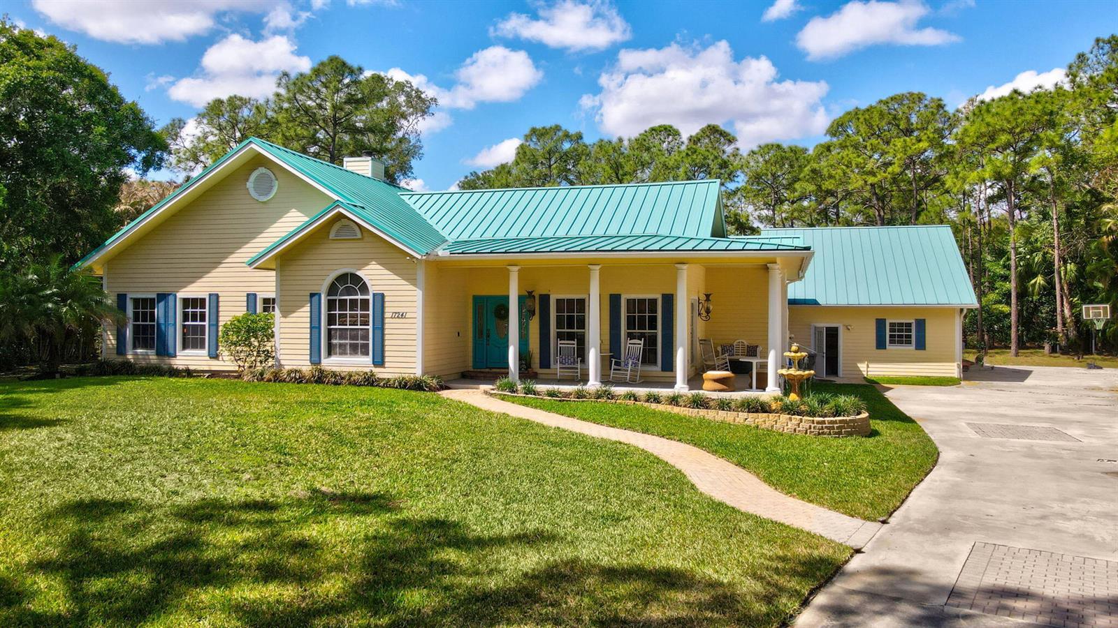A yellow house with a teal metal roof and a front porch sits on a lawn — 17241 N 123rd Ter Terrace N, FL 33478, FL