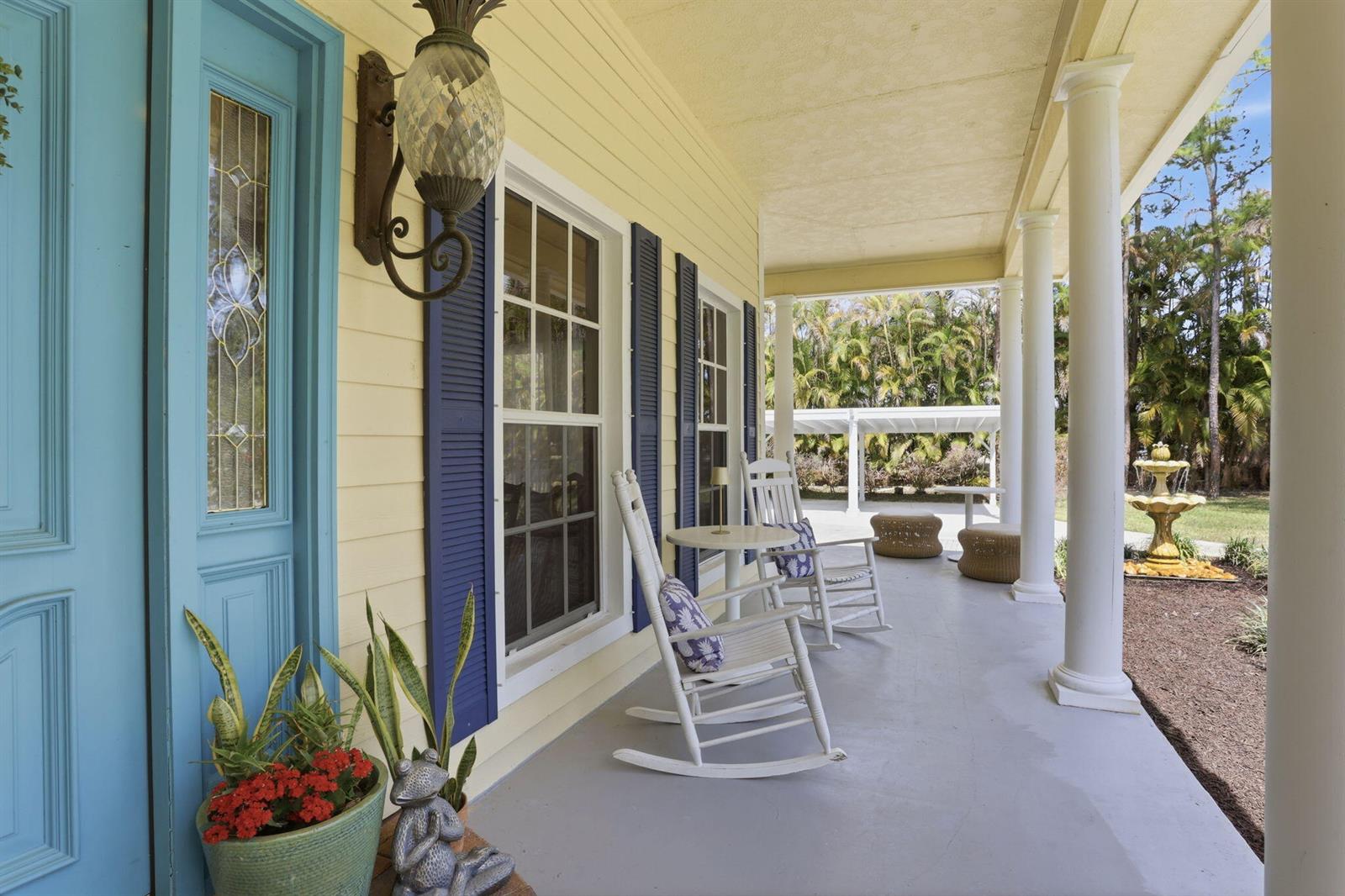 A covered porch features yellow siding, blue shutters, white rocking chairs, and a fountain outside — 17241 N 123rd Ter Terrace N, FL 33478, FL