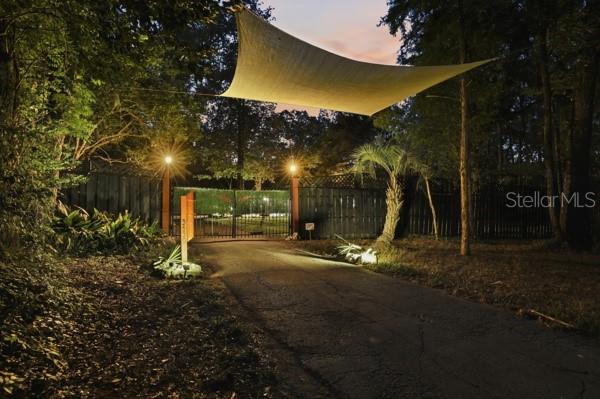 A paved driveway leads to a gated entrance illuminated by lights under a shade sail — 3630 NW 136TH STREET, GAINESVILLE, FL