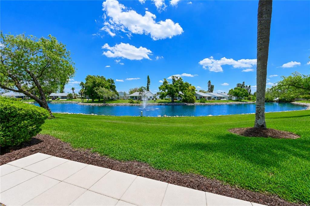 A view of a grassy lawn and a pond with a fountain behind a patio — 4857 INDEPENDENCE DRIVE, BRADENTON, FL