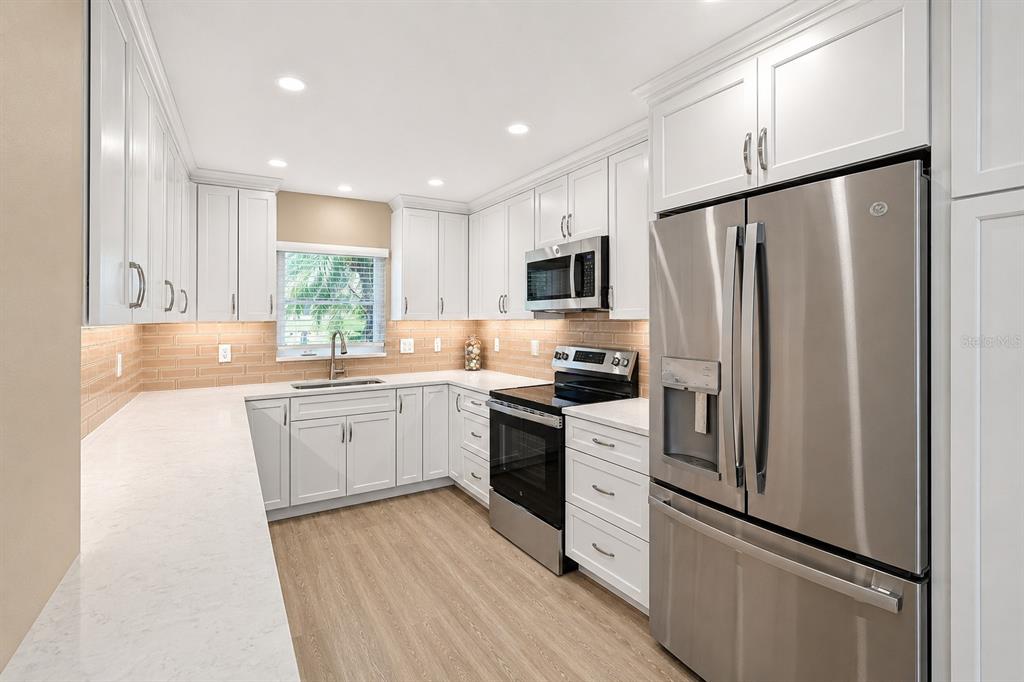 A modern kitchen features white cabinets, stainless steel appliances, and light-colored countertops — 4857 INDEPENDENCE DRIVE, BRADENTON, FL
