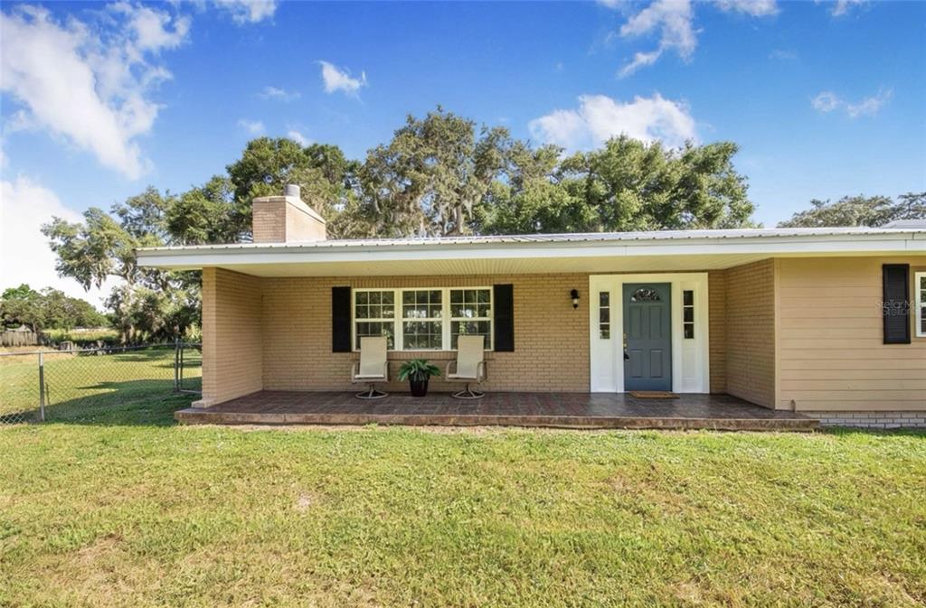 A single-story brick house features a covered front porch, a blue door, and large trees — 4854 E HINSON AVENUE, HAINES CITY, FL