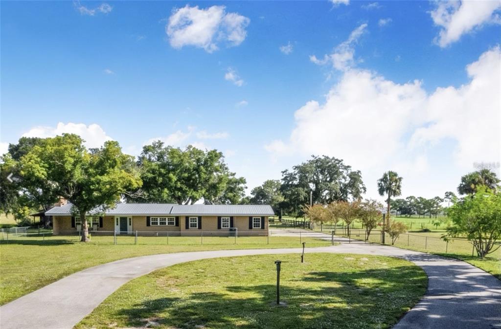 A single-story brick house with a metal roof sits behind a circular driveway — 4854 E HINSON AVENUE, HAINES CITY, FL