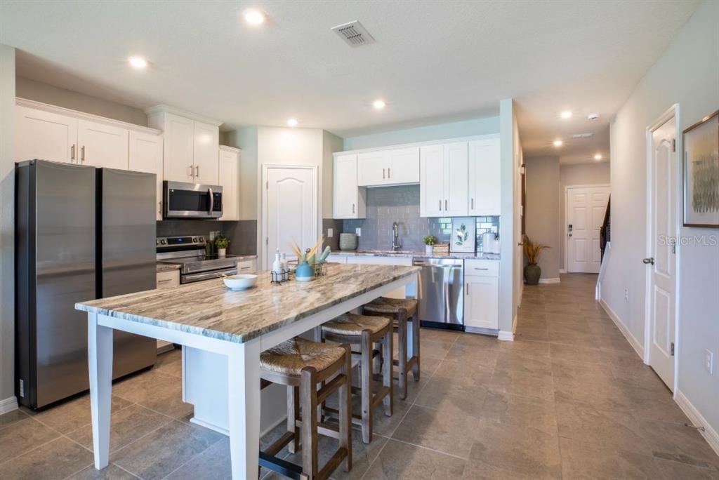 A kitchen features white cabinets, stainless steel appliances, and a large stone-topped island with stools — 10667 IRONWOOD TREE WAY, SAN ANTONIO, FL