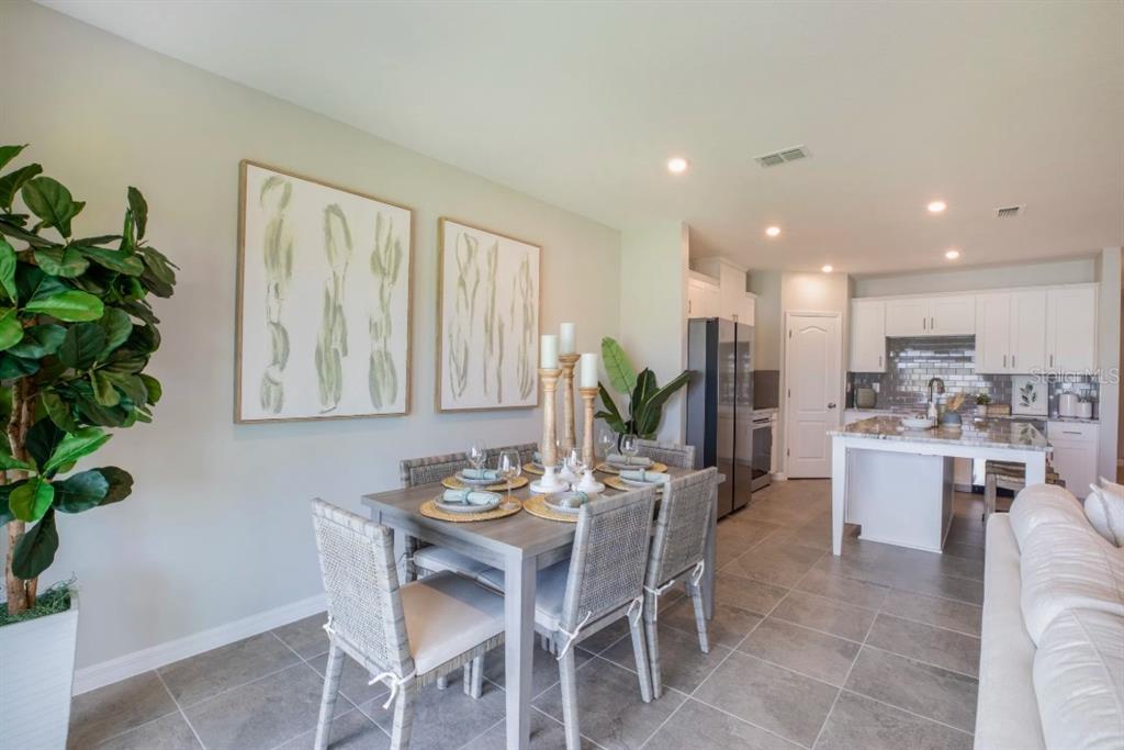 A dining area with a gray table and chairs sits adjacent to an open-concept kitchen — 10667 IRONWOOD TREE WAY, SAN ANTONIO, FL