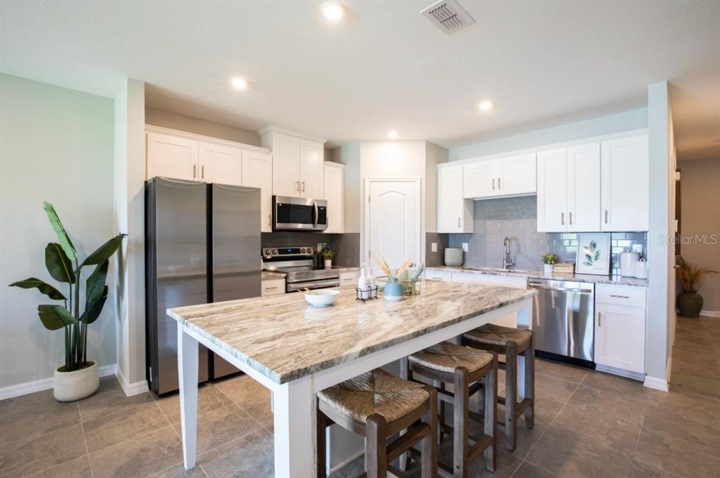 A kitchen features white cabinets, stainless steel appliances, a stone island, and tile flooring — 10667 IRONWOOD TREE WAY, SAN ANTONIO, FL