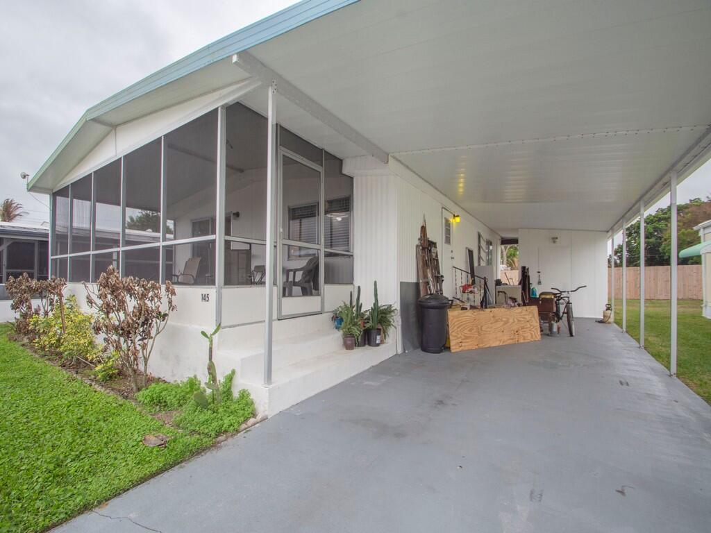 A mobile home exterior featuring a screened-in porch, a large carport, and a concrete driveway — 4800 SE Federal Highway # 145, Stuart FL 34997, STUART, FL