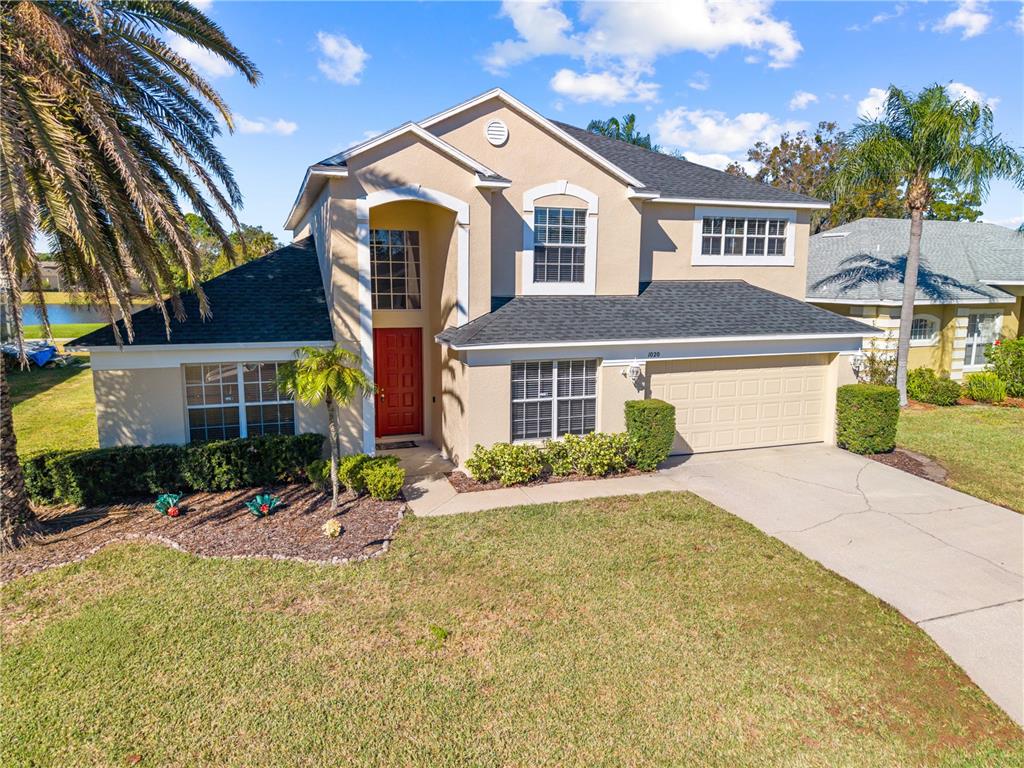 A two-story tan house with a red front door, a garage, and a palm tree — 1020 GOLF COURSE PARKWAY, DAVENPORT, FL