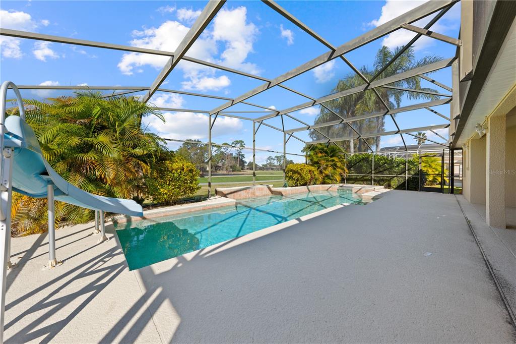 A screened-in pool patio features a blue slide, concrete decking, and views of a golf course — 1020 GOLF COURSE PARKWAY, DAVENPORT, FL