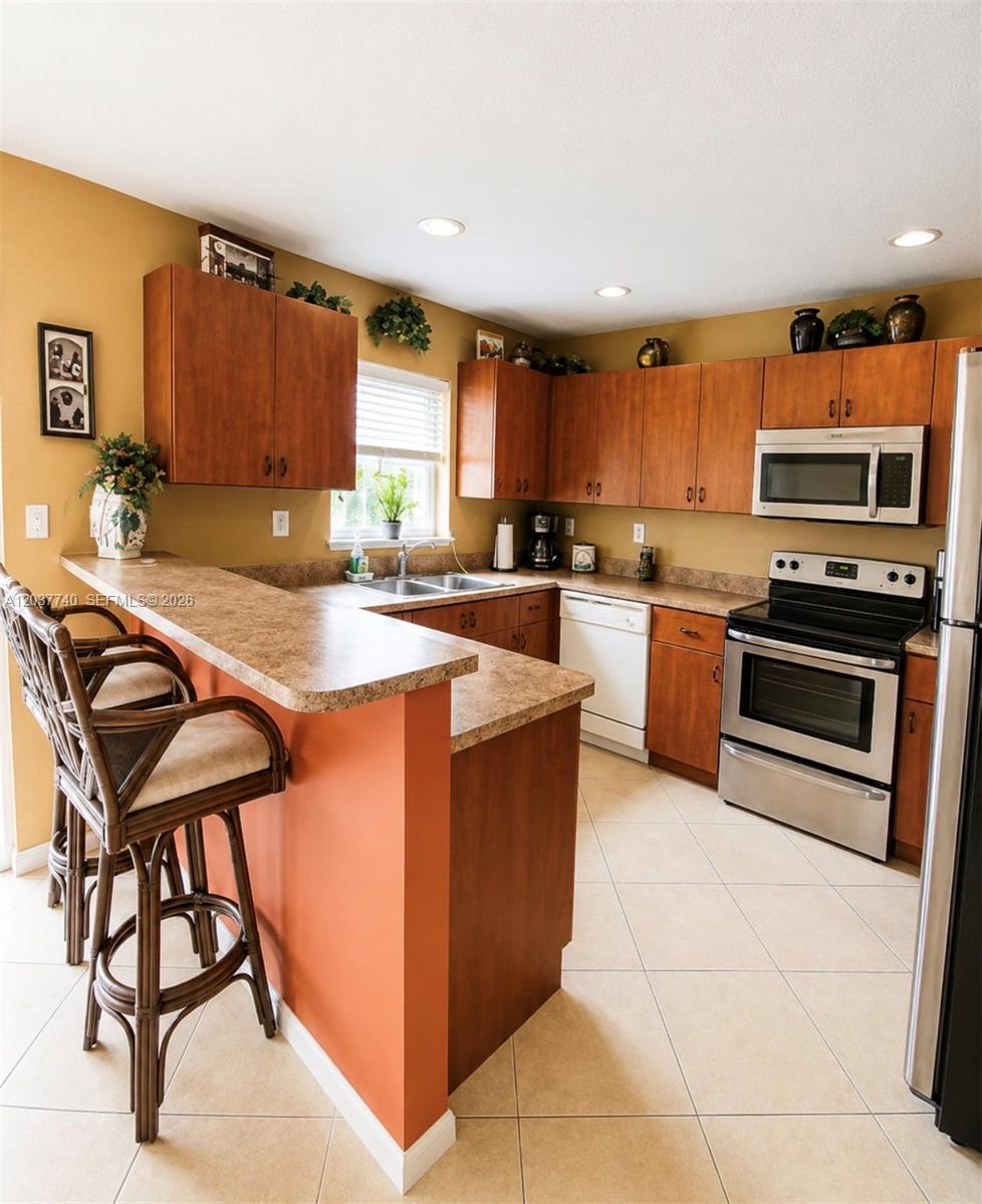 A kitchen features wood cabinets, stainless steel appliances, a breakfast bar, and tile flooring — 16355 SW 46th Ter # 16355, Miami FL 33185, MIAMI, FL