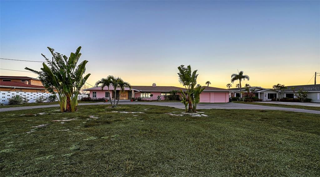 A pink, single-story house with a large lawn and palm trees at sunset — 7322 WESTMORELAND DRIVE, SARASOTA, FL