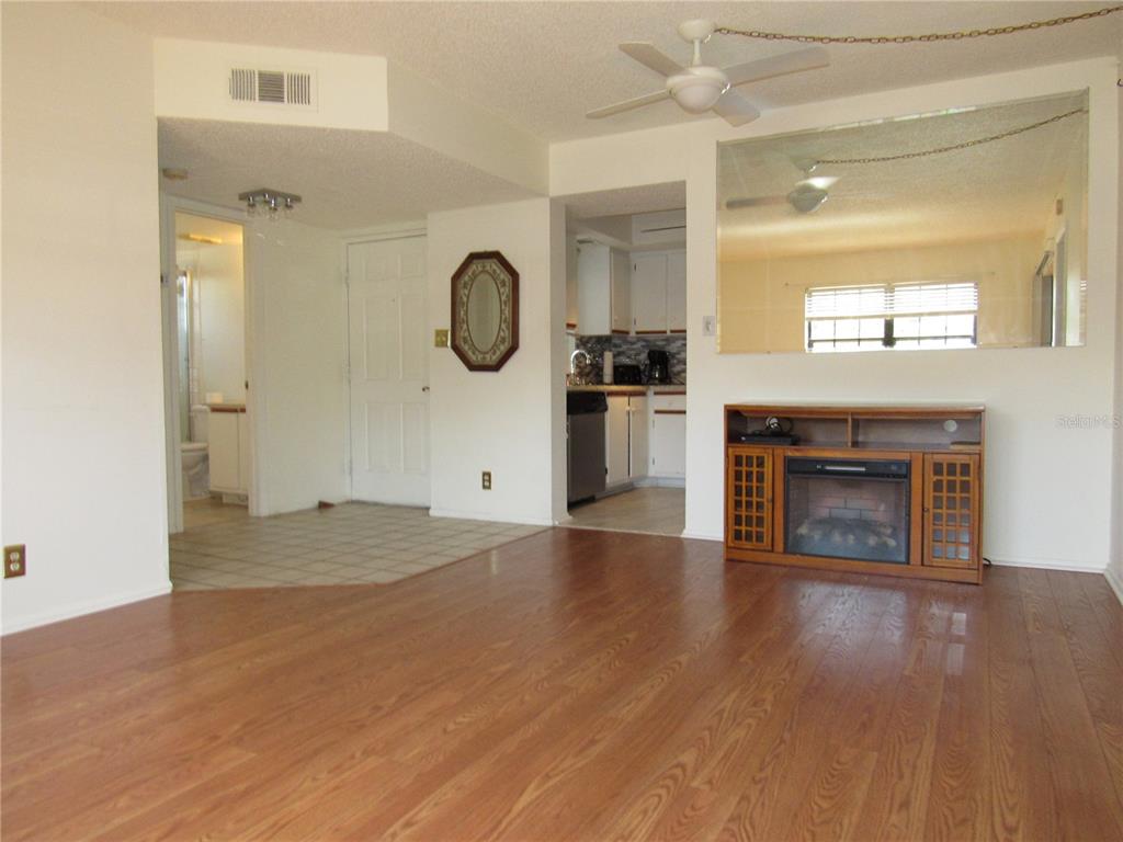 A living room features wood-look flooring, a fireplace console, a ceiling fan, and a mirror — 19505 QUESADA AVENUE UNIT PP101, PORT CHARLOTTE, FL