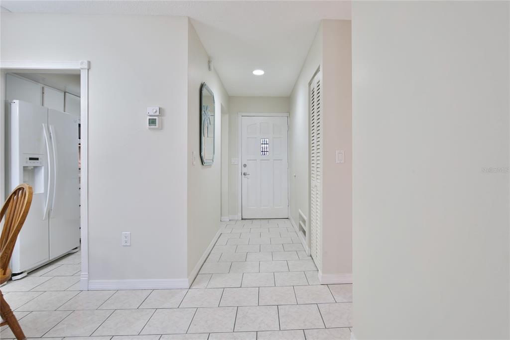 A tiled hallway leads to a white front door with a view of a kitchen — 4612 PARK ACRES DRIVE, BRADENTON, FL