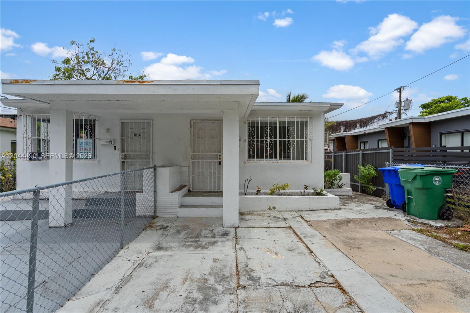 The exterior of a single-story white house features a concrete driveway and a chain-link fence — 370 NE 55th St, Miami FL 33137, MIAMI, FL