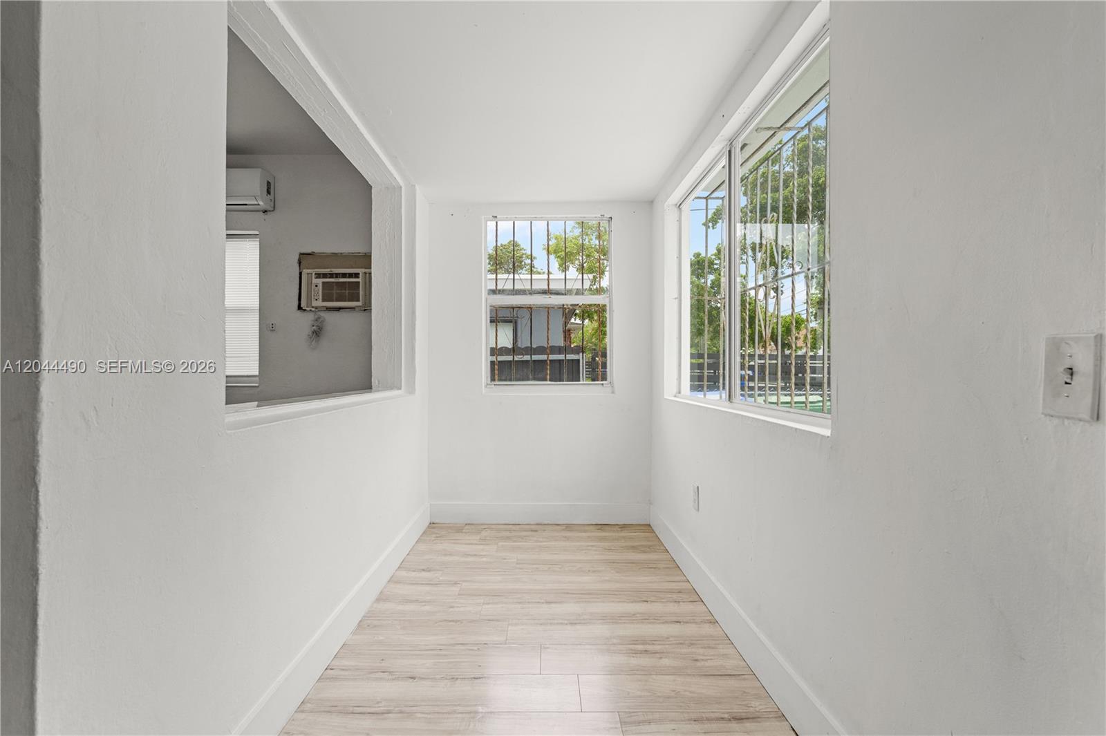 A narrow, white-walled room features light wood-look flooring and windows with security bars — 370 NE 55th St, Miami FL 33137, MIAMI, FL