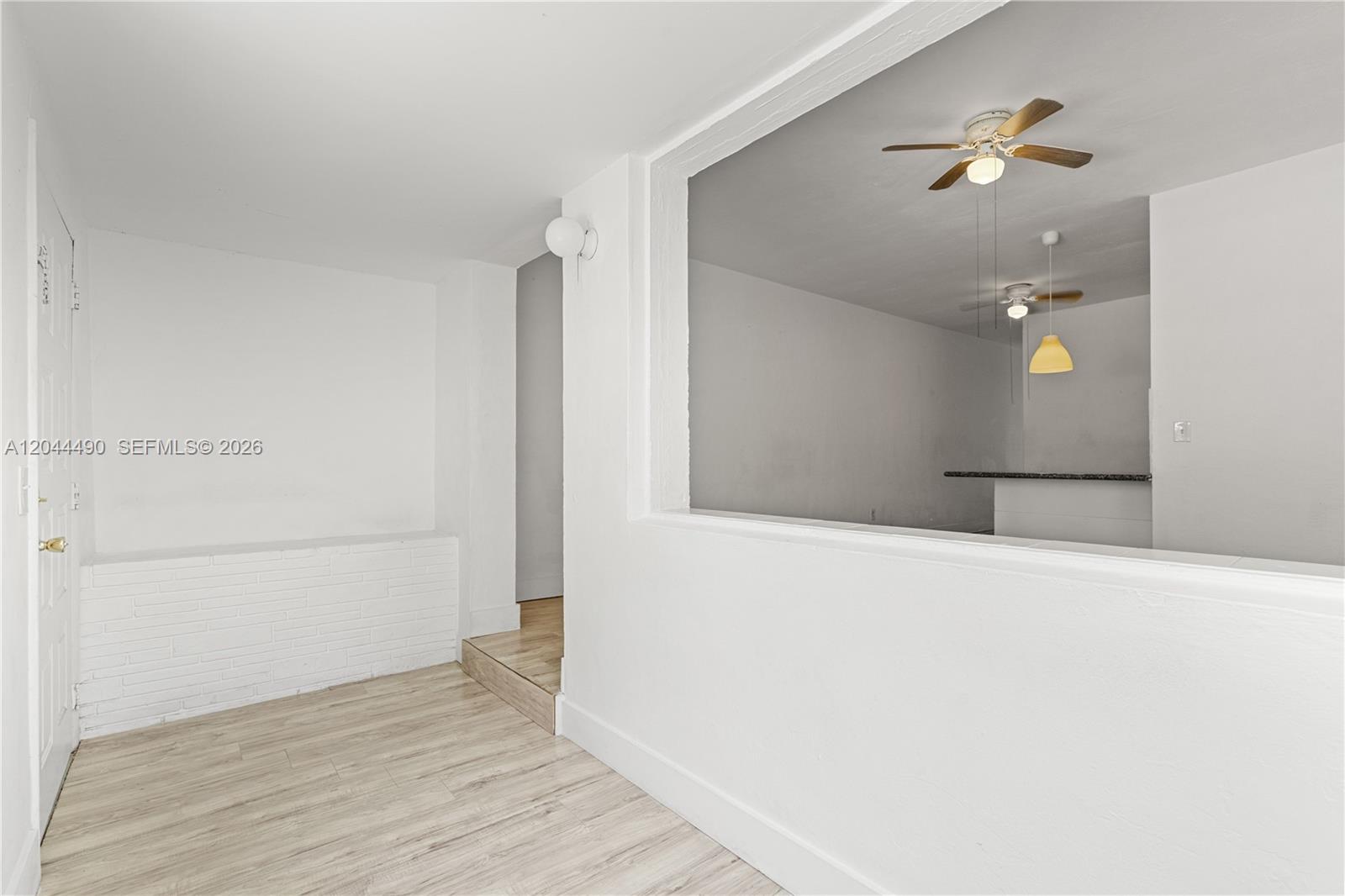 A white room with light wood flooring features a large rectangular opening into a kitchen — 370 NE 55th St, Miami FL 33137, MIAMI, FL