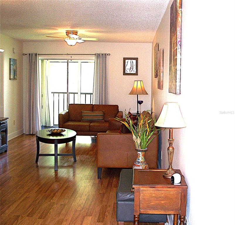 A living room with wood-look flooring, brown leather furniture, and a sliding glass balcony door — 3808 N OAK DRIVE UNIT U42, TAMPA, FL