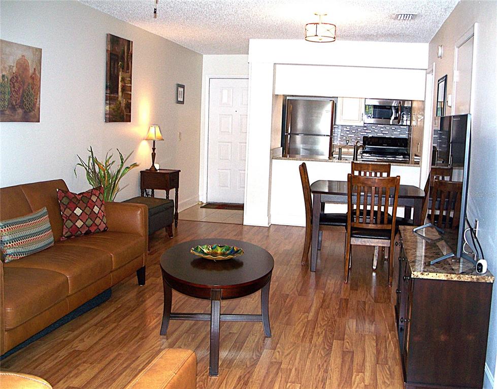 A living room and dining area with wood-look flooring, a leather sofa, and kitchen access — 3808 N OAK DRIVE UNIT U42, TAMPA, FL