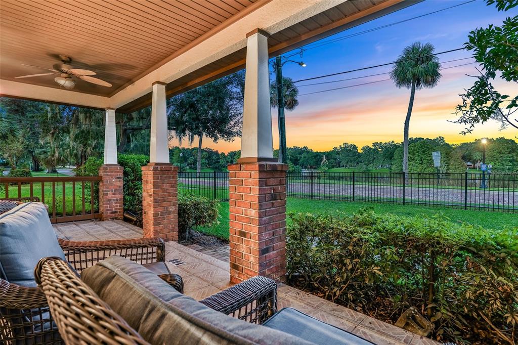 A covered porch with brick columns overlooks a fenced lawn and a sunset sky — 148 S THORNTON AVENUE, ORLANDO, FL