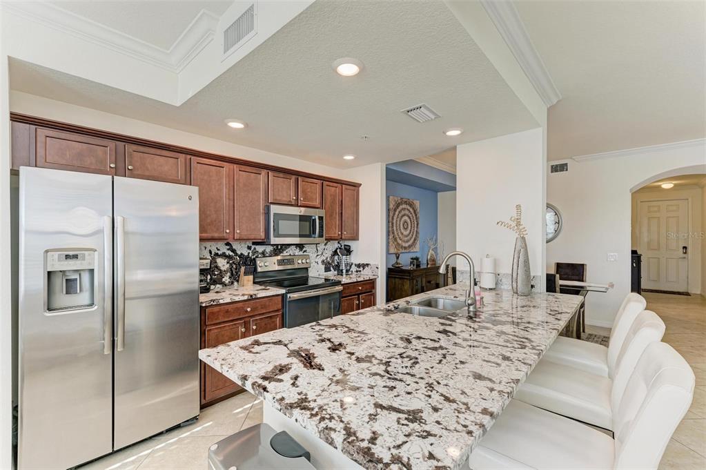 A kitchen features dark wood cabinets, granite countertops, a stainless steel refrigerator, and bar seating — 16814 VARDON TERRACE UNIT 103, BRADENTON, FL